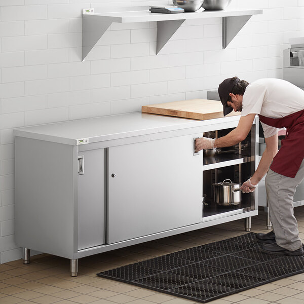 A man using a Regency stainless steel enclosed base table in a professional kitchen.