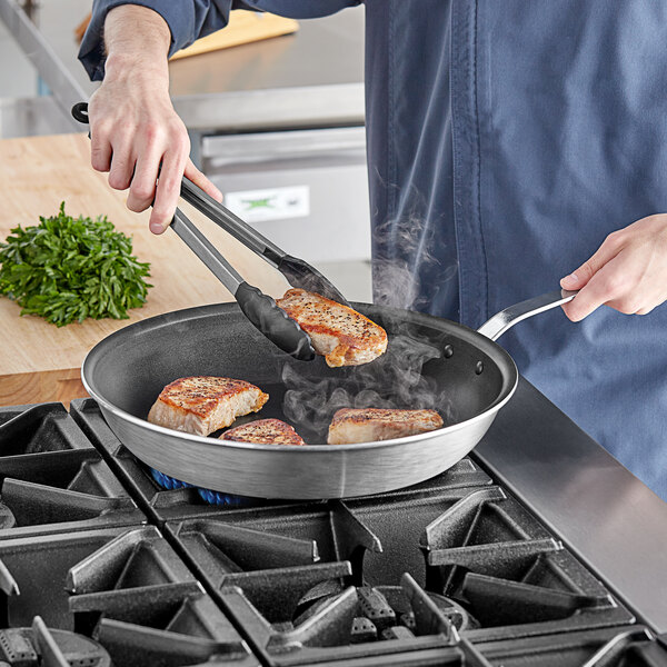 A person cooking food in a Vollrath Wear-Ever non-stick fry pan on a stove.