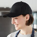 A woman in a professional kitchen wearing a black Mercer Culinary baseball cap.