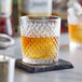 An Acopa Aurelius rocks glass filled with amber liquid on a stone coaster.
