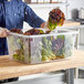 A person using a Choice clear polycarbonate food storage box to hold lettuce on a white counter.