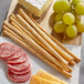 Panealba Thin Grissini Breadsticks and grapes on a wooden surface.